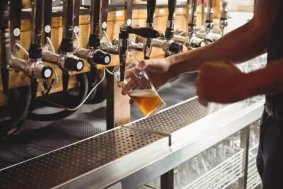 Mid section of bar tender filling beer from bar pump at bar counter